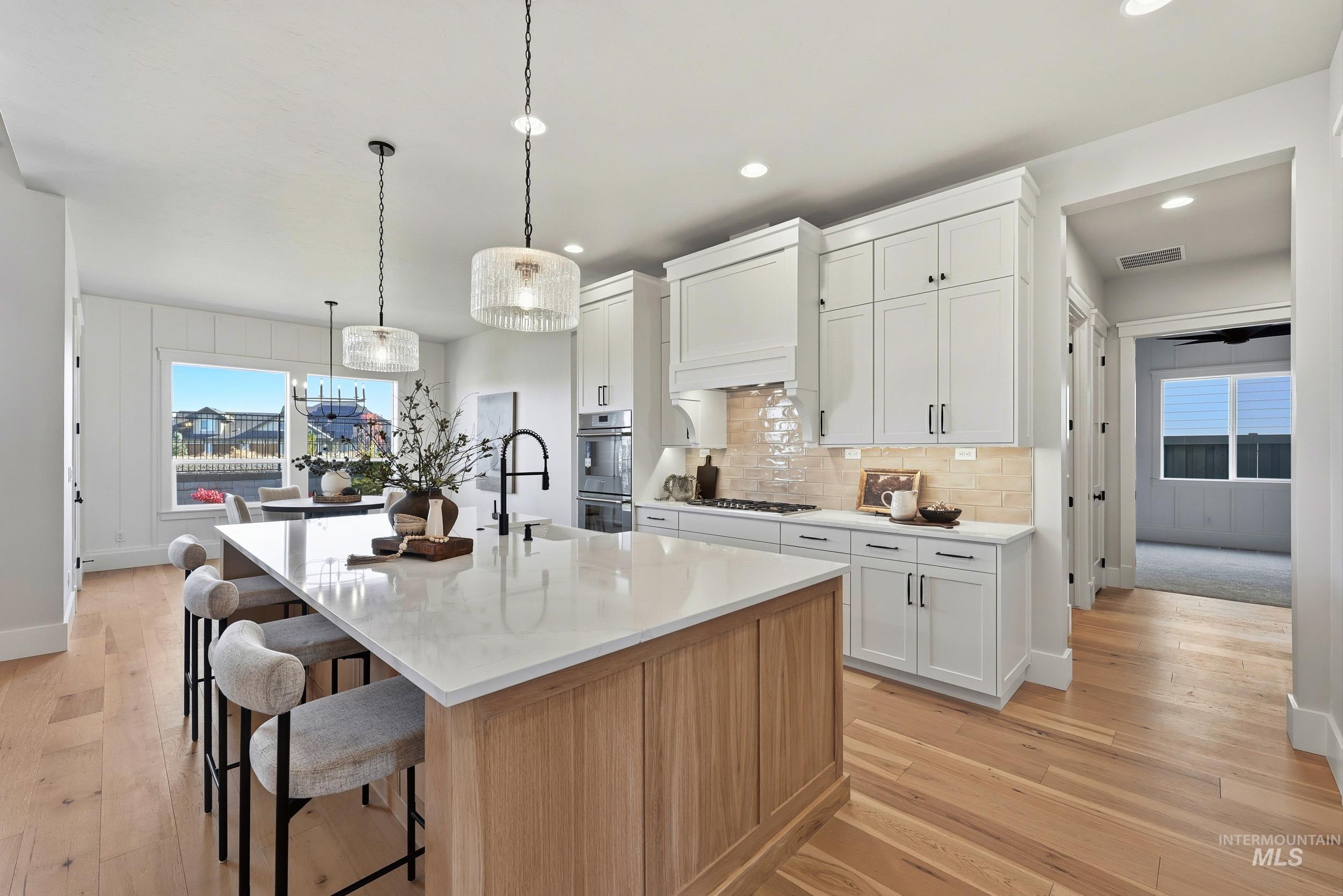 6771 South Messner Way Meridian, ID 83642 - Photo 18 of 45 Kitchen with white cabinets, light wood-type flooring, a center island with sink, backsplash, and recessed lighting