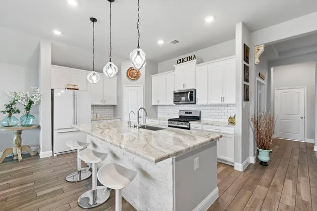 a kitchen with stainless steel appliances kitchen island granite countertop a stove a refrigerator a sink a dining table and chairs with wooden floor
