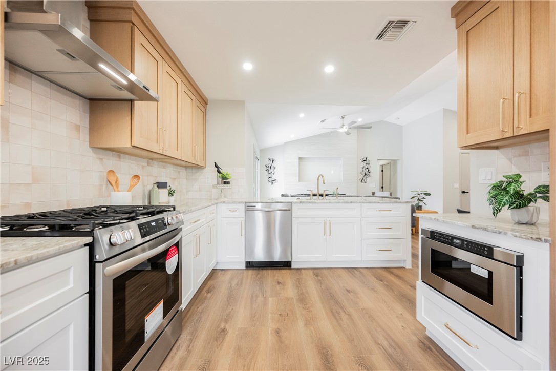 9337 Quail Ridge Drive Las Vegas, NV 89134 - Photo 16 of 28 Kitchen with decorative backsplash, stainless steel appliances, wall chimney exhaust hood, vaulted ceiling, and light wood-style flooring