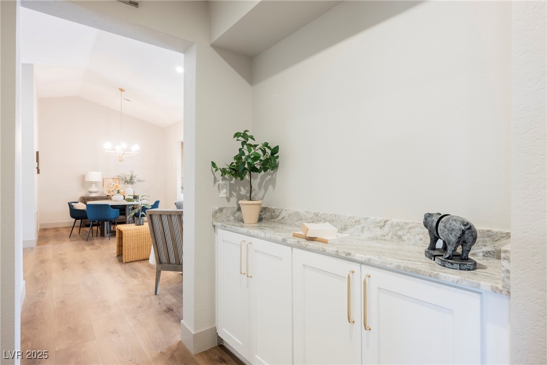 9337 Quail Ridge Drive Las Vegas, NV 89134 - Photo 20 of 28 Bar area featuring white cabinetry, vaulted ceiling, pendant lighting, light stone counters, and light wood-type flooring