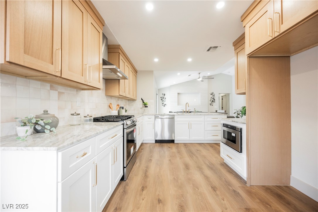 9337 Quail Ridge Drive Las Vegas, NV 89134 - Photo 5 of 28 Kitchen with backsplash, appliances with stainless steel finishes, light stone countertops, wall chimney exhaust hood, and lofted ceiling