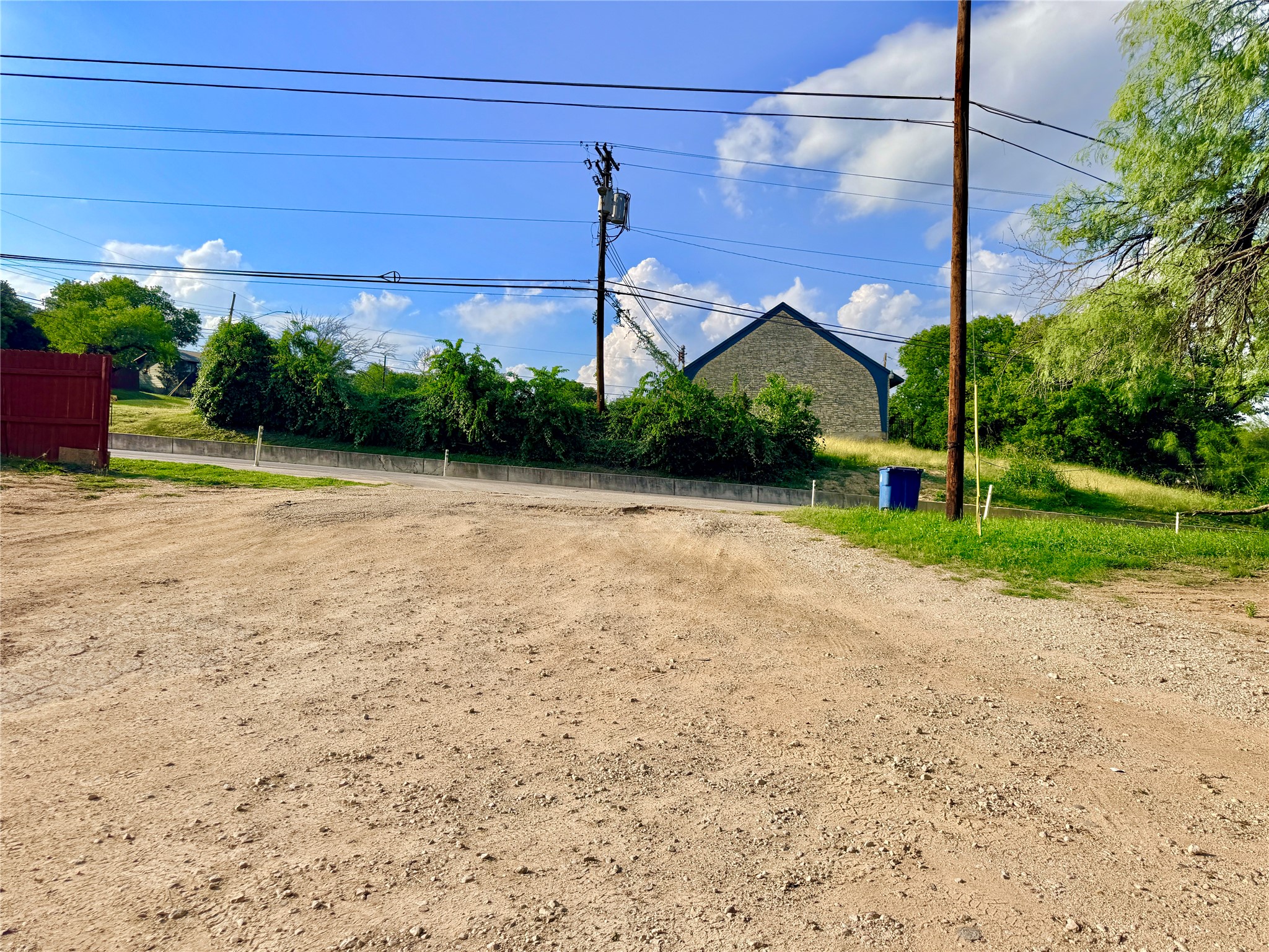 6257 Manor Road, Unit B Austin, TX 78723 - Photo 38 of 38 Expansive gravel lot with a red wood fence, bordered by mature trees and a sloped grassy area