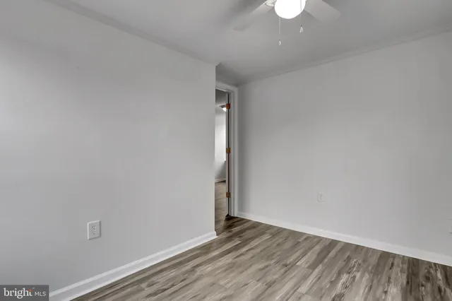 a view of an empty room with wooden floor and a ceiling fan