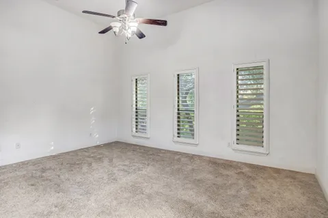 an empty room with chandelier fan and windows