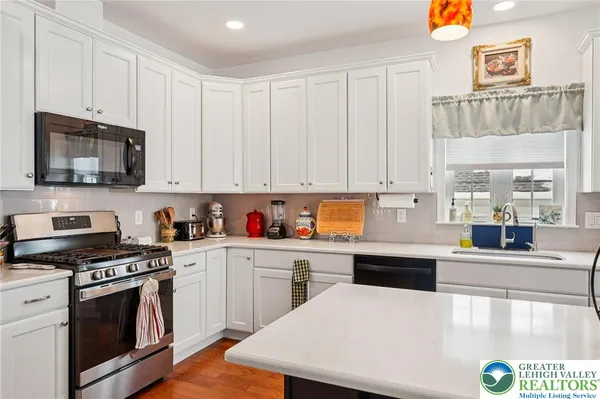 a kitchen with granite countertop a stove top oven a sink dishwasher and white cabinets with wooden floor