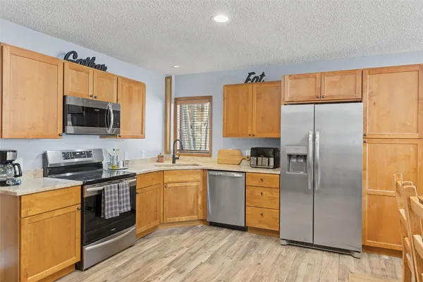 a kitchen with stainless steel appliances granite countertop a refrigerator a stove top oven a sink dishwasher and wooden cabinets with wooden floor