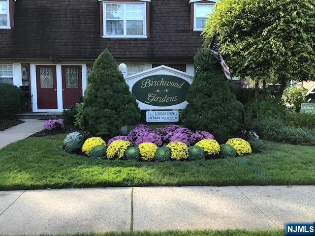 a front view of a house with lots of trees and flowers
