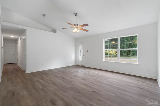 an empty room with wooden floor chandelier fan and windows