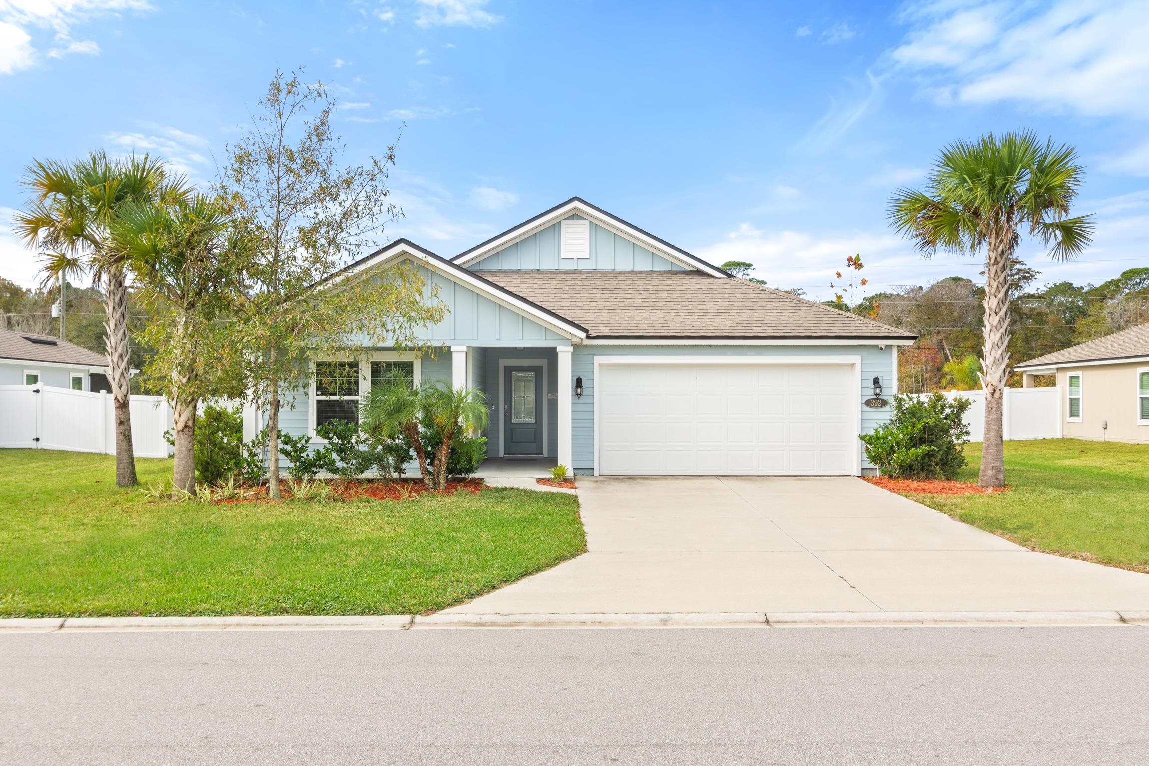 a view of a white house next to a yard with big trees and plants
