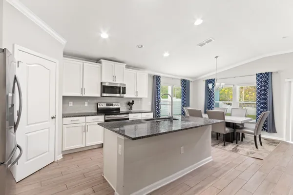 a kitchen with stainless steel appliances granite countertop a stove a sink a refrigerator and white cabinets with wooden floor