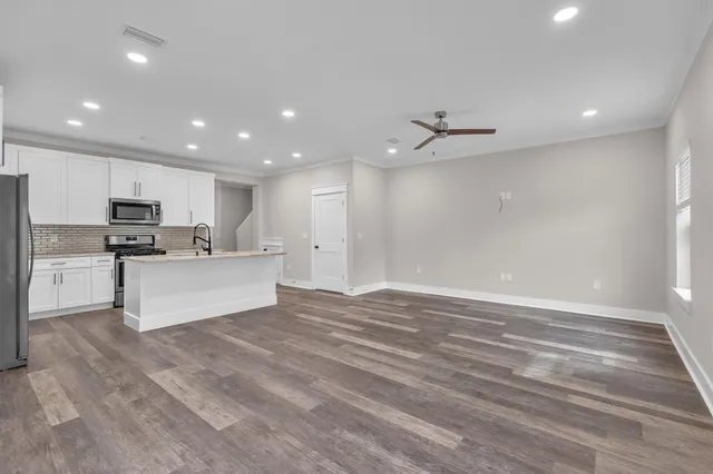 a large white kitchen with kitchen island a stove a sink a refrigerator and white cabinets with wooden floor