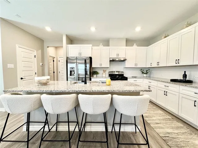 a kitchen with stainless steel appliances kitchen island granite countertop a table chairs sink and cabinets