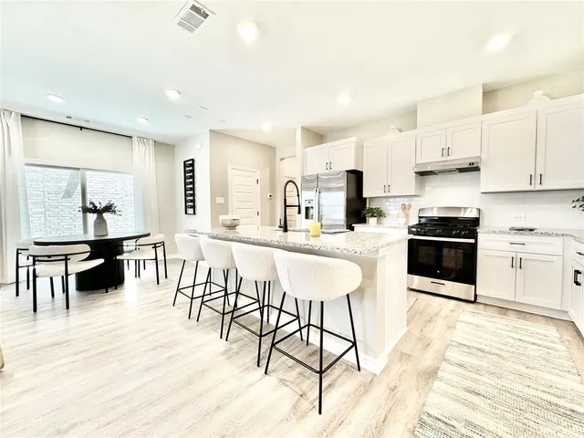 a kitchen with stainless steel appliances kitchen island granite countertop a stove a sink a dining table and chairs with wooden floor