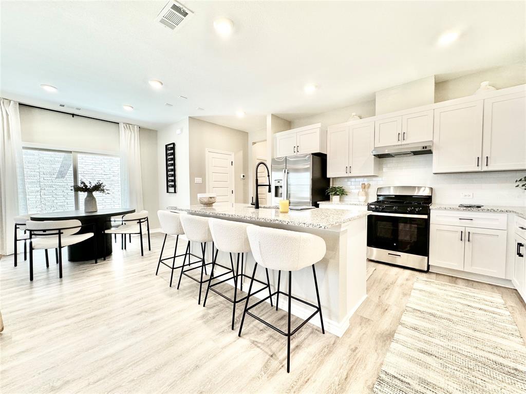 8523 Leyton Road The Colony, TX 75056 - Photo 9 of 39 a kitchen with stainless steel appliances kitchen island granite countertop a stove a sink a dining table and chairs with wooden floor