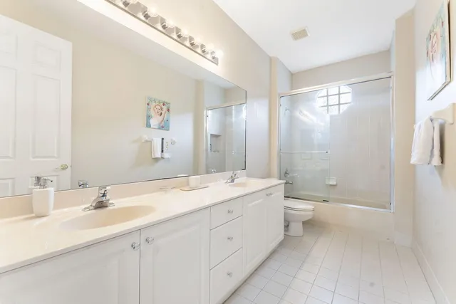 a bathroom with a double vanity sink toilet mirror and windows