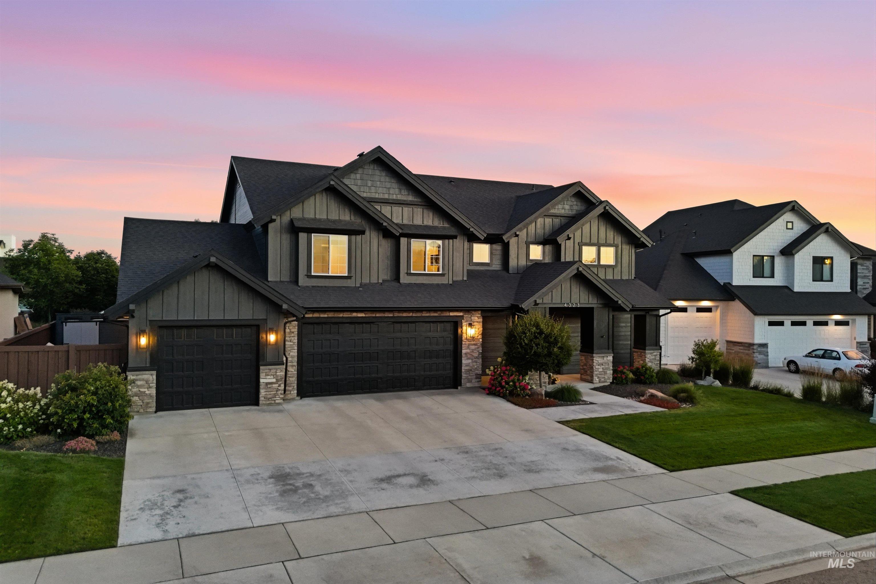 4323 West Ladle Rpds Drive Meridian, ID 83646 - Photo 4 of 49 Contemporary residence featuring a dark gray exterior with vertical and horizontal siding, a multi-gabled roofline, stone accents, a three-car garage, and established front landscaping