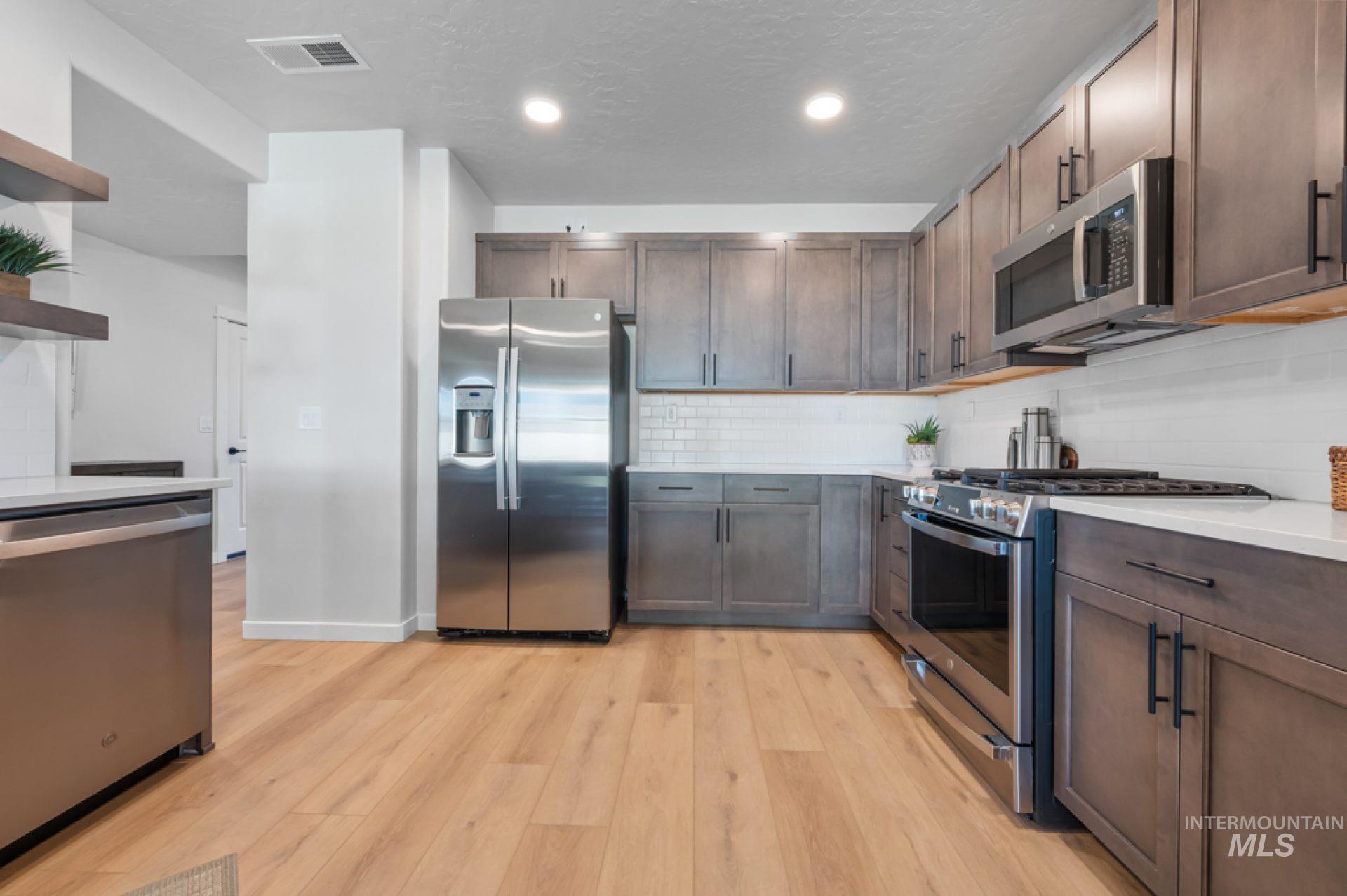 3347 East Fitz Roy Street Kuna, ID 83634 - Photo 3 of 15 Kitchen featuring stainless steel appliances, tasteful backsplash, light wood finished floors, light stone counters, and dark brown cabinetry