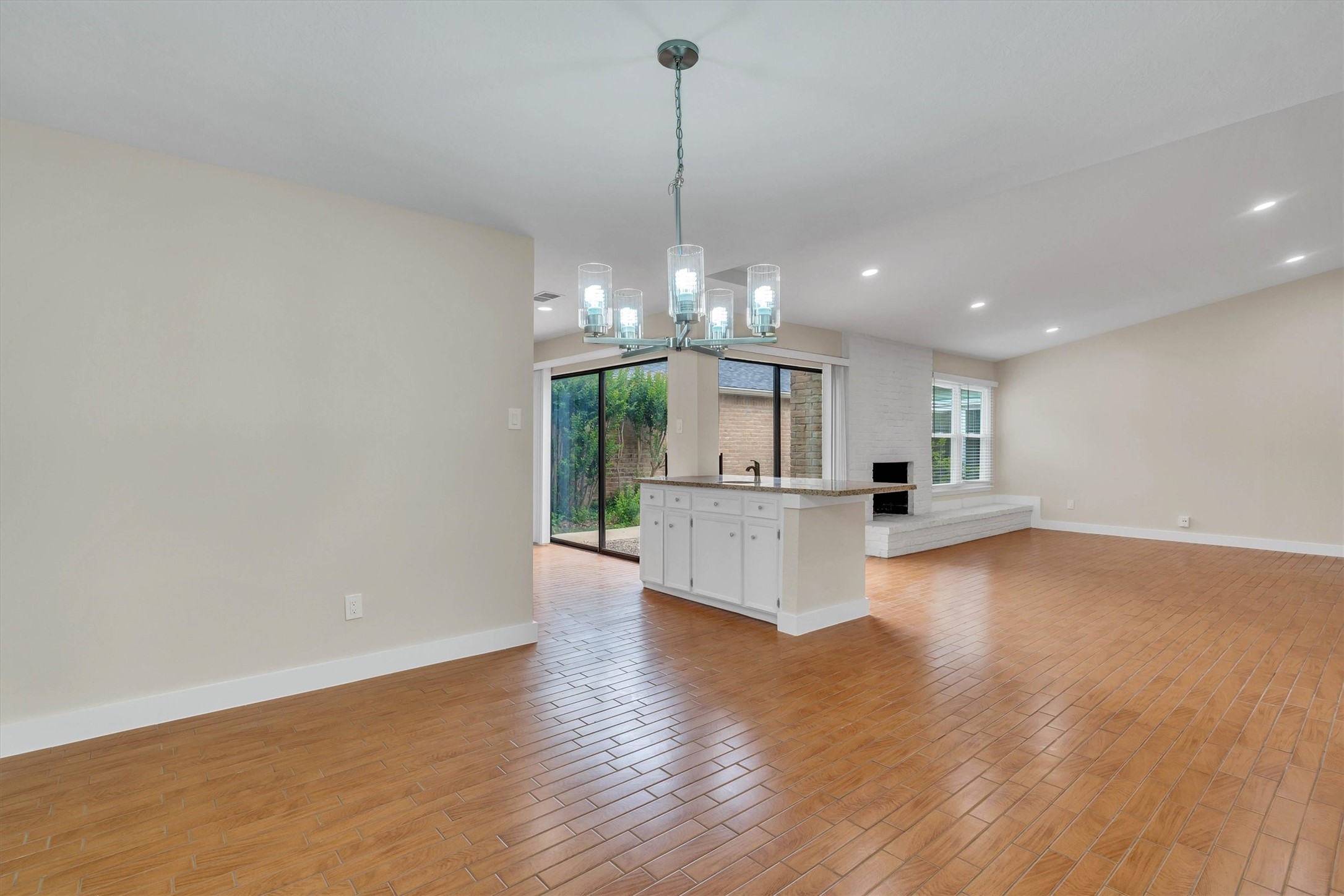 2163 Paso Rello Drive Houston, TX 77077 - Photo 12 of 45 This open-concept living space features a modern kitchen island with pendant lighting, wood-look tile flooring, and a cozy fireplace. Large windows and sliding glass doors offer natural light and outdoor access.