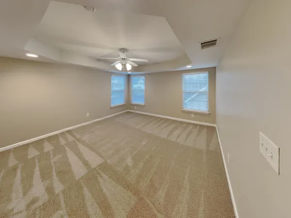 an empty room with chandelier fan and windows