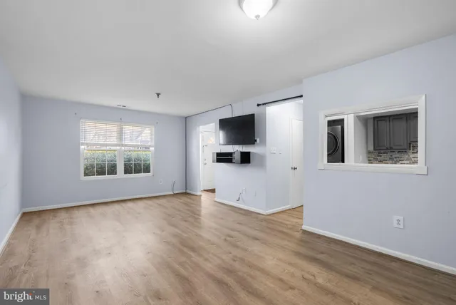 a view of an empty room with window and hardwood floor