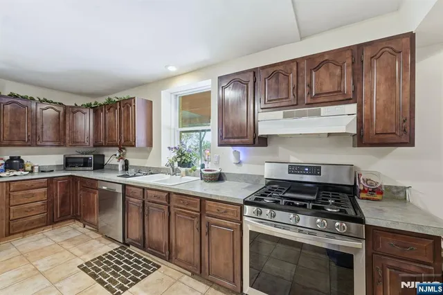 a kitchen with stainless steel appliances granite countertop a stove top oven a sink dishwasher and cabinets with wooden floor