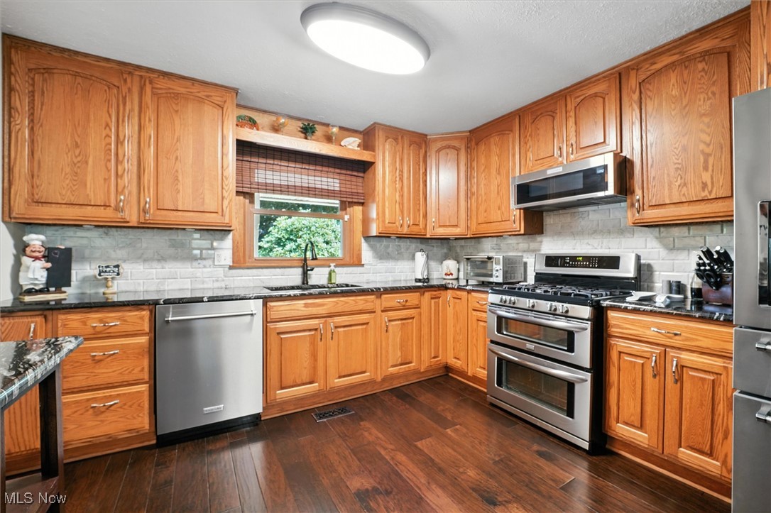 2930 South Ridge Road East Kingsville, OH 44048 - Photo 7 of 49 Kitchen featuring appliances with stainless steel finishes, dark wood finished floors, brown cabinetry, and decorative backsplash