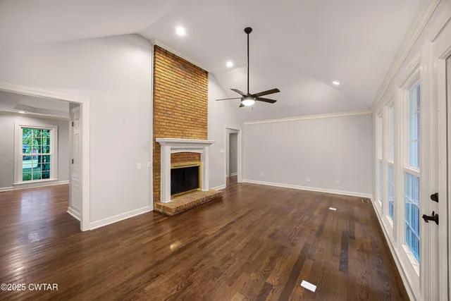 an empty room with wooden floor fireplace and windows