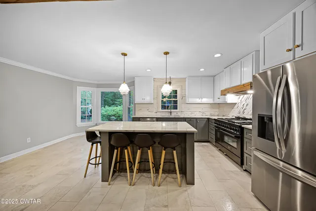 a kitchen with stainless steel appliances granite countertop a sink a stove a refrigerator and island with wooden floor