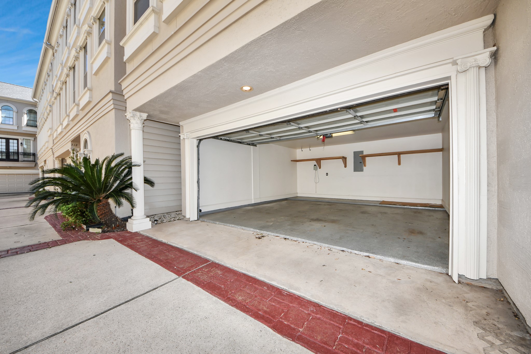 710 Jackson Hill Street Houston, TX 77007 - Photo 28 of 31 Spacious, clean two-car garage with built-in shelving. It features a smooth concrete floor, white walls, and an automatic garage door. The exterior is part of a well-maintained building with decorative columns and a small landscaped area.