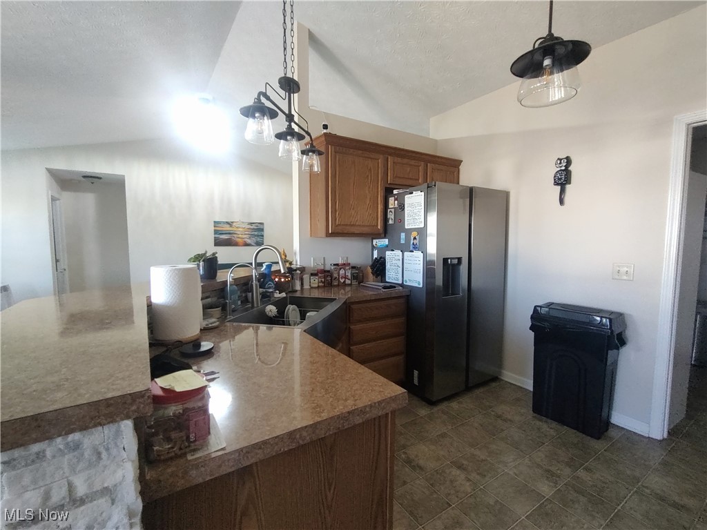 870 Susan Road Ravenna, OH 44266 - Photo 18 of 35 Kitchen with lofted ceiling, a peninsula, stainless steel refrigerator with ice dispenser, brown cabinetry, and hanging light fixtures