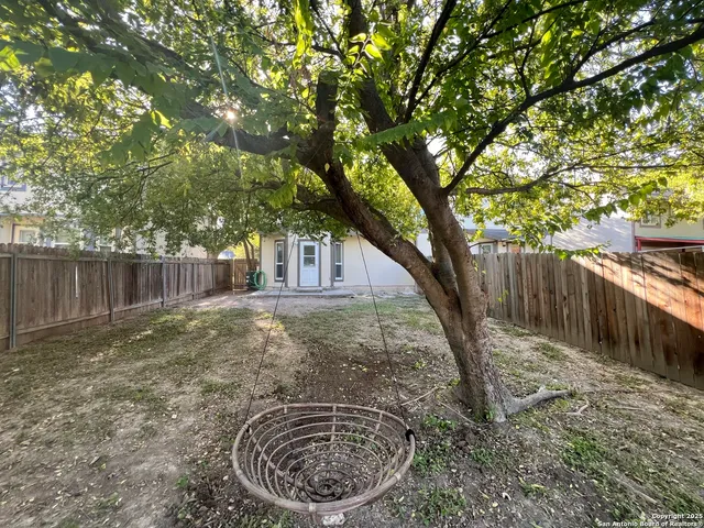 a view of a backyard with large trees and wooden fence