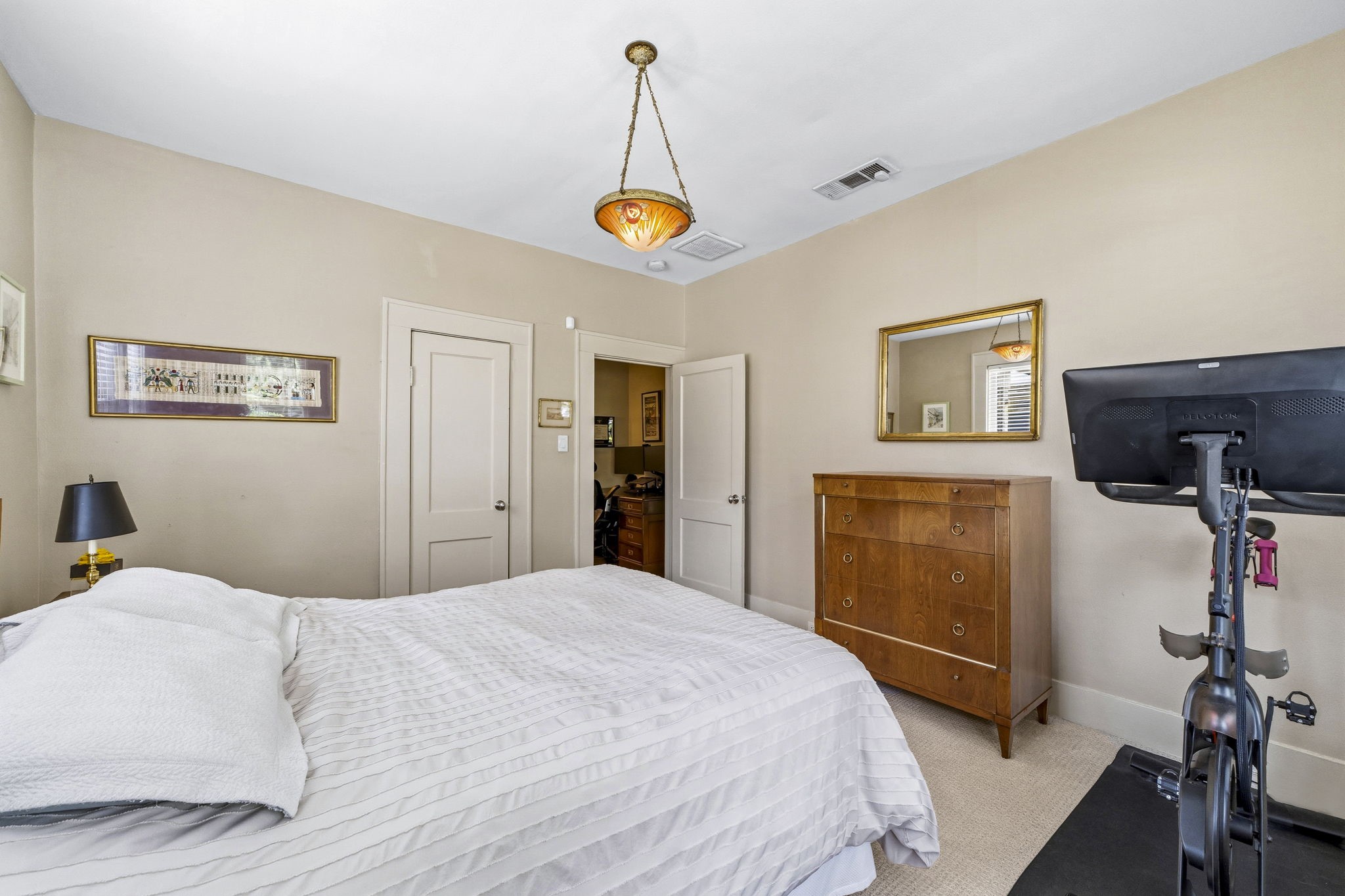 1521 Kipling Street Houston, TX 77006 - Photo 31 of 35 This cozy bedroom features neutral walls, a comfortable bed, wooden dresser, and an exercise bike. It also includes a modern light fixture and a wall mirror, creating a warm and practical space.