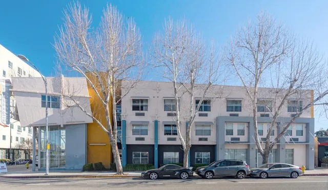 a front view of a building with lot of cars and trees