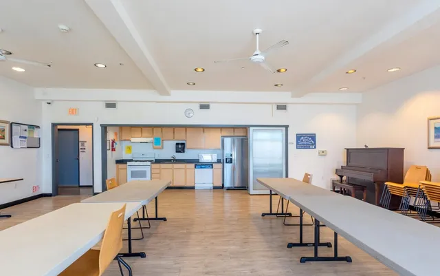 a room with stainless steel appliances kitchen island granite countertop lots of white furniture a refrigerator and wooden floors