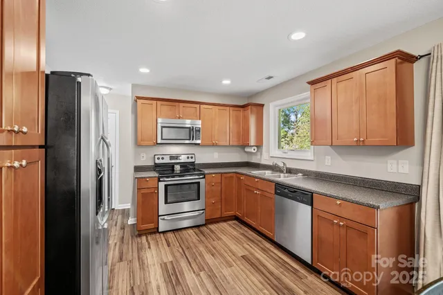 a kitchen with stainless steel appliances granite countertop a refrigerator a sink dishwasher a stove and white countertops with wooden floor