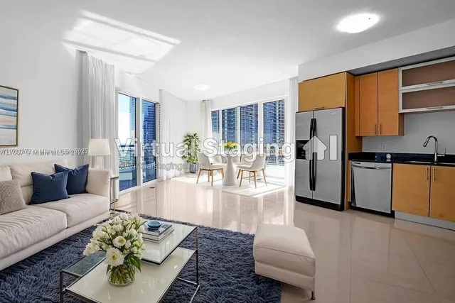 a living room with stainless steel appliances furniture wooden floor and a kitchen view