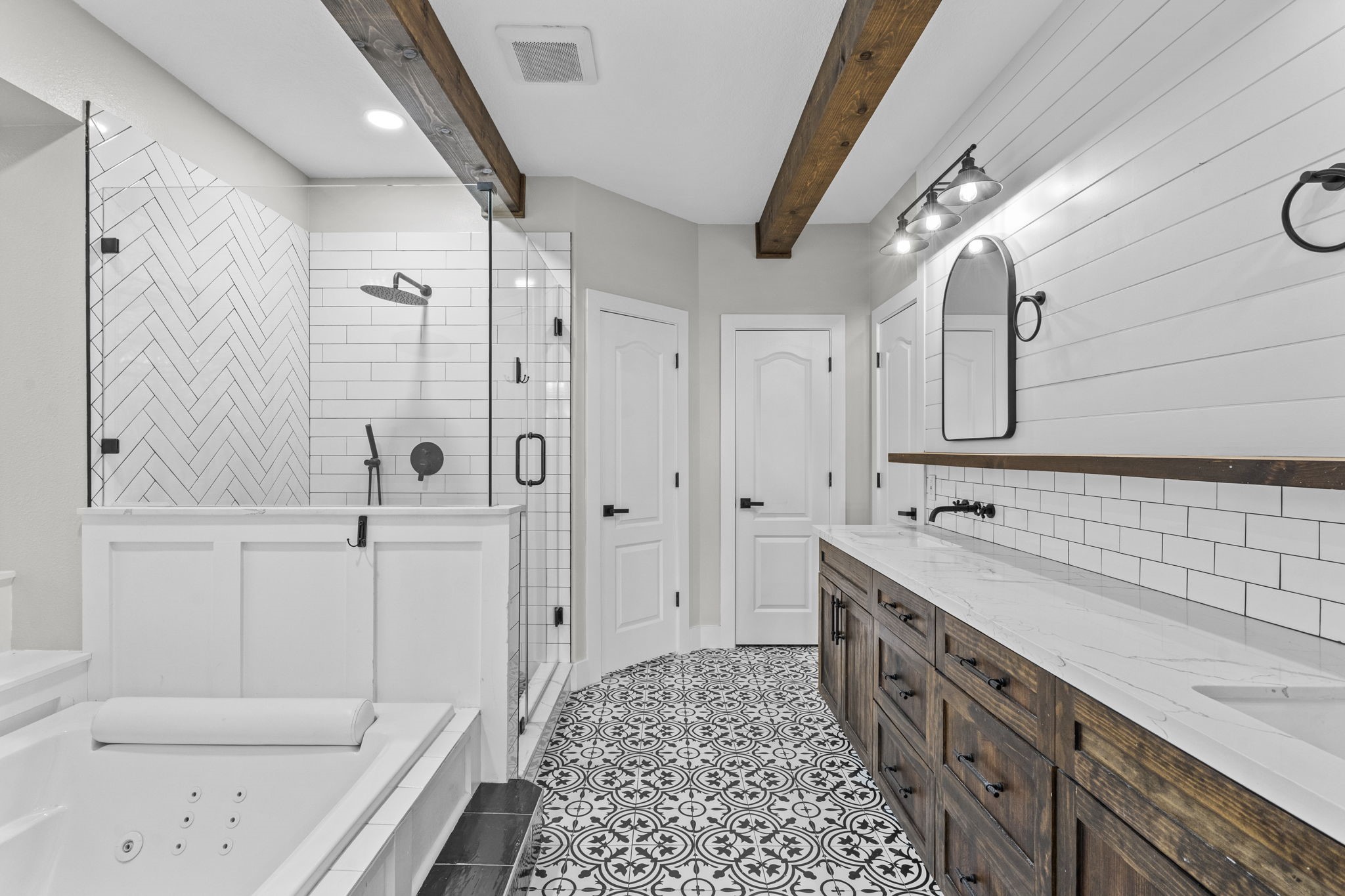 2730 Lawrence Road Kemah, TX 77565 - Photo 24 of 46 This bathroom features a modern farmhouse design with a spacious walk-in shower and a soaking tub. It has a dual vanity with rustic wood cabinets, patterned tile flooring, and white shiplap walls accented by dark fixtures and a wooden beam.