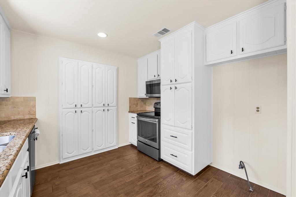 141 Travis Lane Hewitt, TX 76643 - Photo 11 of 31 Kitchen featuring wood-finish flooring, white cabinetry, integrated stainless steel appliances, speckled countertops, and a full-height tile backsplash