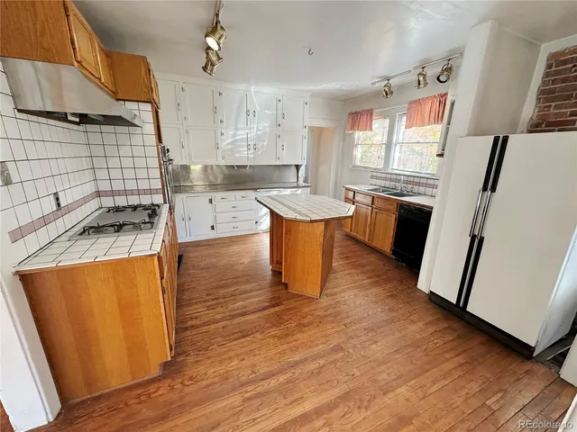 a kitchen with stainless steel appliances granite countertop a refrigerator a sink dishwasher a stove and white countertops with wooden floor