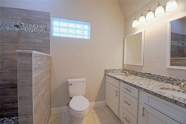 a bathroom with a granite countertop toilet a sink a mirror and a shower