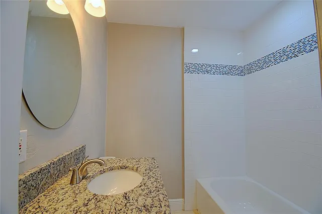 a bathroom with a granite countertop sink a mirror and a bathtub