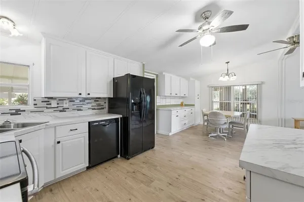 a kitchen with stainless steel appliances kitchen island granite countertop a refrigerator a sink dishwasher a stove with white cabinets and wooden floor