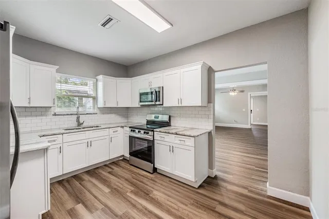 a kitchen with stainless steel appliances granite countertop a stove a sink dishwasher and a refrigerator with white cabinets