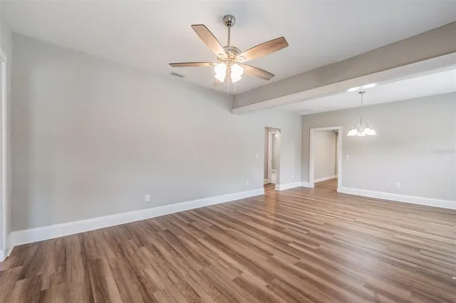 a view of an empty room with wooden floor and a ceiling fan