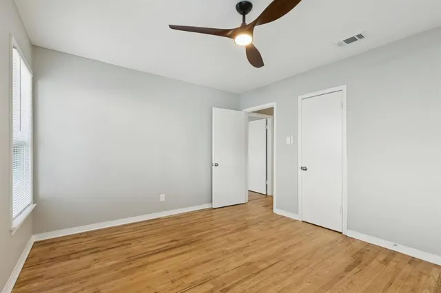 an empty room with wooden floor ceiling fan and window