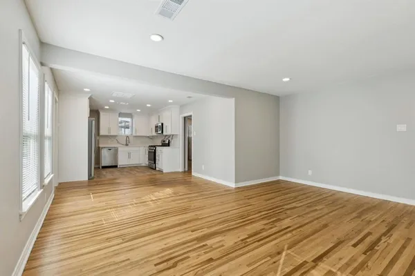 a view of an empty room with wooden floor and a kitchen