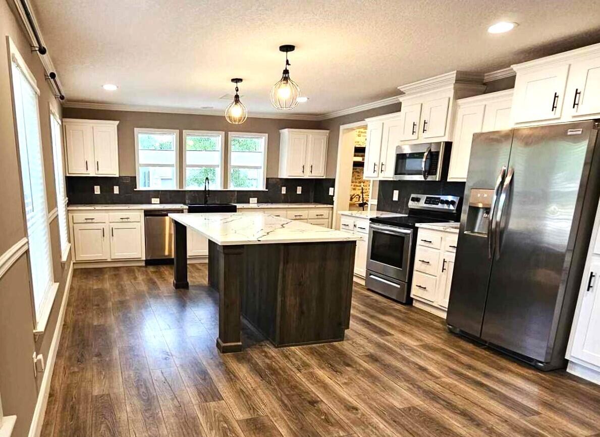a kitchen with stainless steel appliances granite countertop a stove a sink dishwasher a refrigerator white cabinets and wooden floor