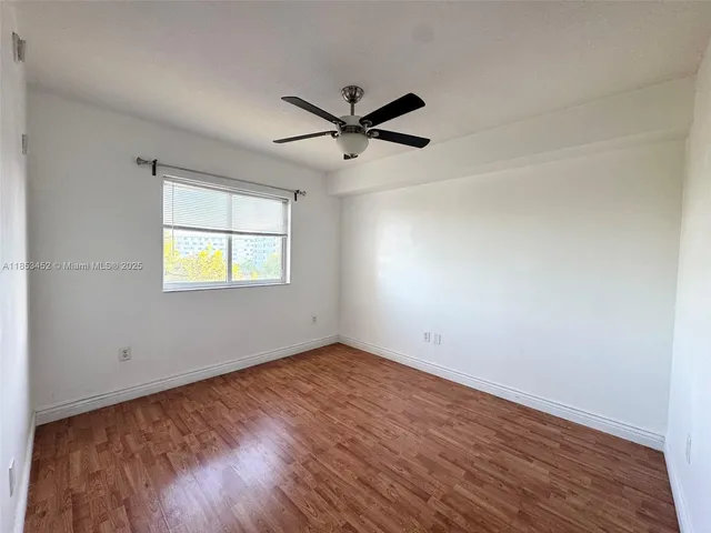 an empty room with wooden floor ceiling fan and windows