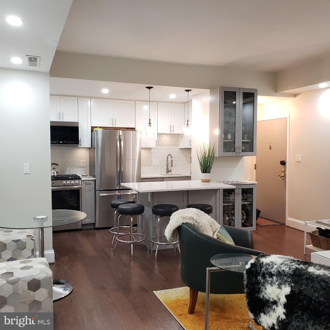 2127 California Street Northwest, Unit 102 Washington, DC 20008 - Photo 3 of 10 a kitchen with stainless steel appliances kitchen island granite countertop a refrigerator a stove a sink and white cabinets with wooden floor