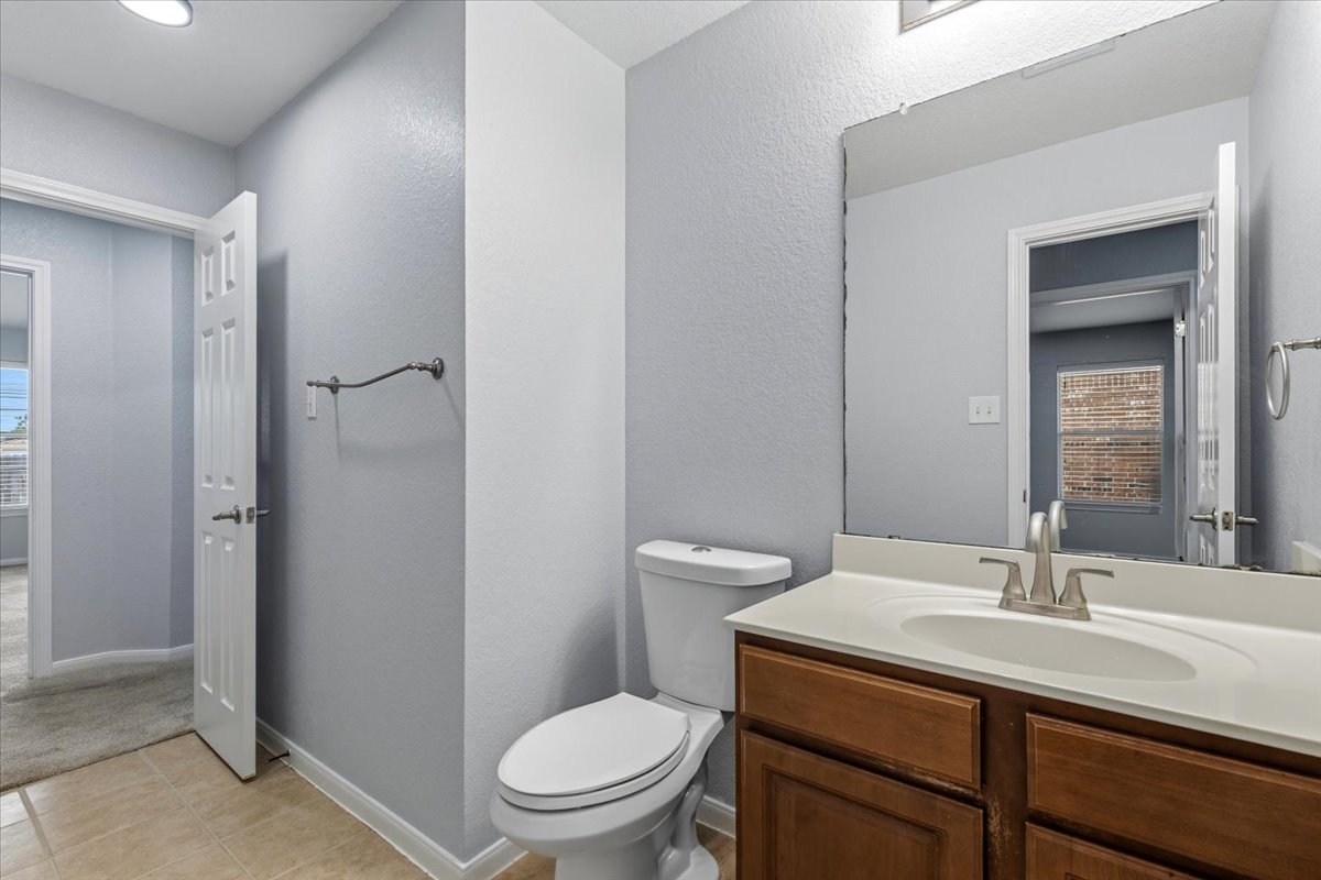 17812 Masi Loop Pflugerville, TX 78660 - Photo 27 of 38 Bathroom featuring a wood-finish vanity with an integrated sink and light-toned countertop, a frameless wall mirror, and neutral-toned floor tiling